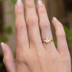 A vintage-inspired yellow sapphire and diamond engagement ring worn on the hand.