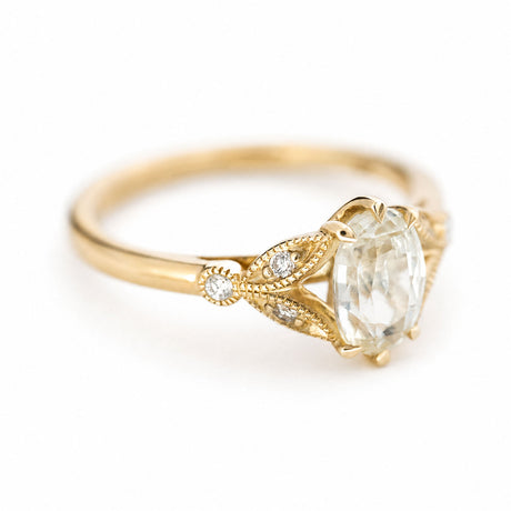 A vintage-inspired yellow gold engagement ring with a pale yellow sapphire at the centre with round brilliant-cut diamond details in the shoulders.