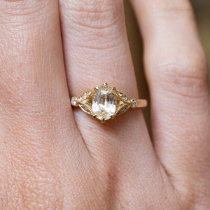 Antique-inspired oval-cut yellow sapphire and diamond engagement ring in yellow gold worn on the finger.