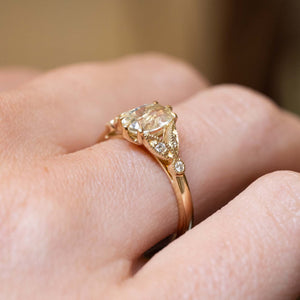 Close detail of an oval-cut yellow sapphire engagement ring with diamond shoulders in polished yellow gold.