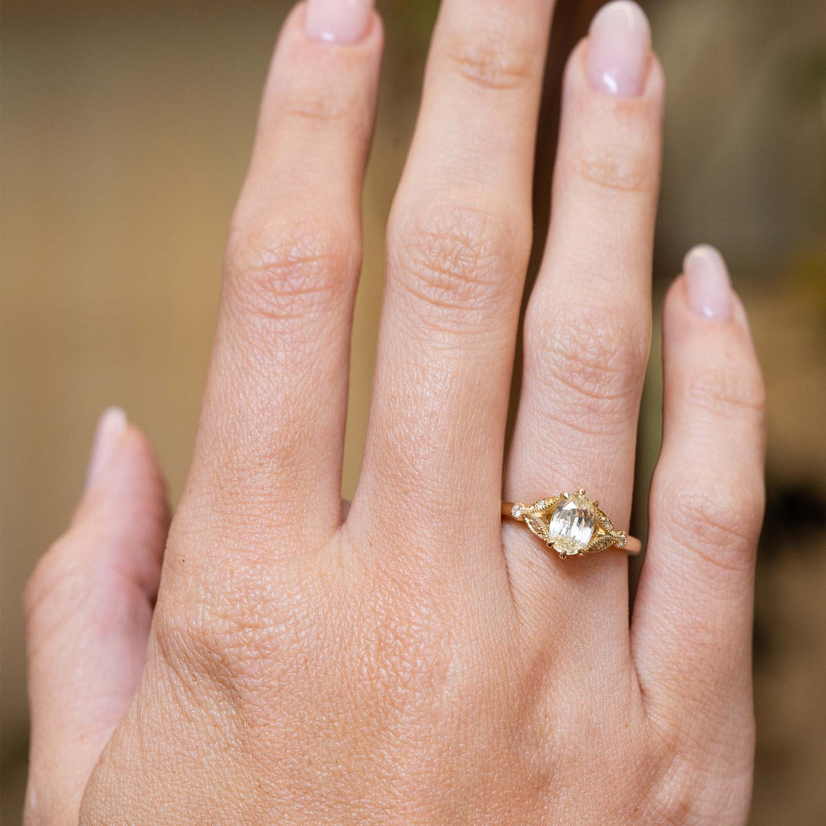Oval-cut yellow sapphire and diamond engagement ring displayed on the hand in a yellow gold setting.