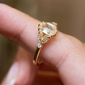 Detailed view of a vintage-inspired yellow gold engagement ring featuring an oval-cut yellow sapphire with diamond accents.