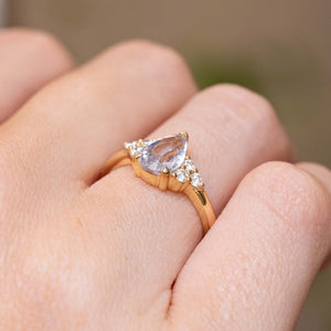 Close detail of a vintage-inspired white pear-cut sapphire engagement ring with a diamond trefoil setting in yellow gold.