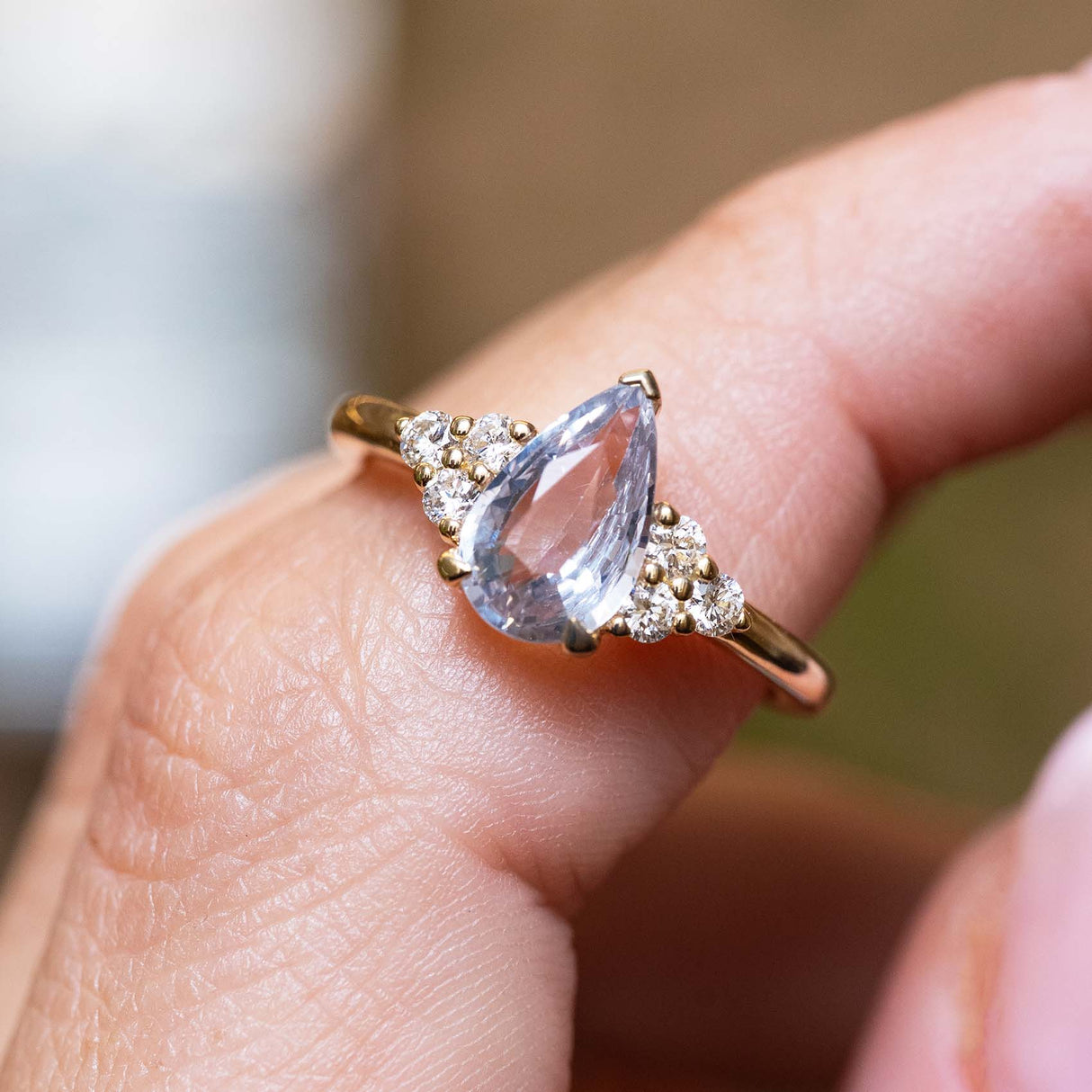 Vintage-inspired yellow gold engagement ring featuring a white pear-cut sapphire with a sparkling diamond trefoil design.