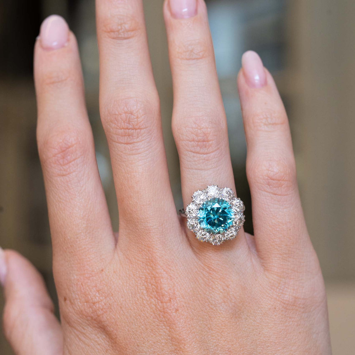 An antique Edwardian zircon and diamond cluster cocktail ring worn on the hand.