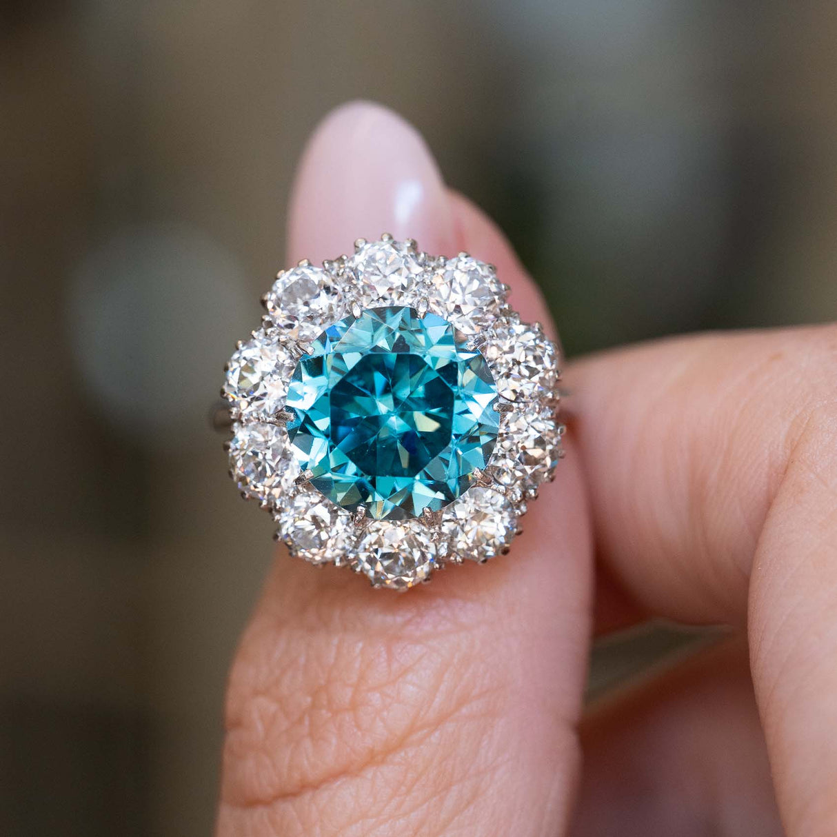 An antique Edwardian zircon and diamond cluster cocktail ring shown on the thumb.