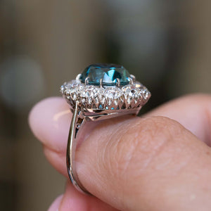 Side detail of an antique Edwardian zircon and diamond cluster cocktail ring held between the fingers.