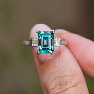An antique Art Deco 1920s zircon and diamond ring held between the fingers.
