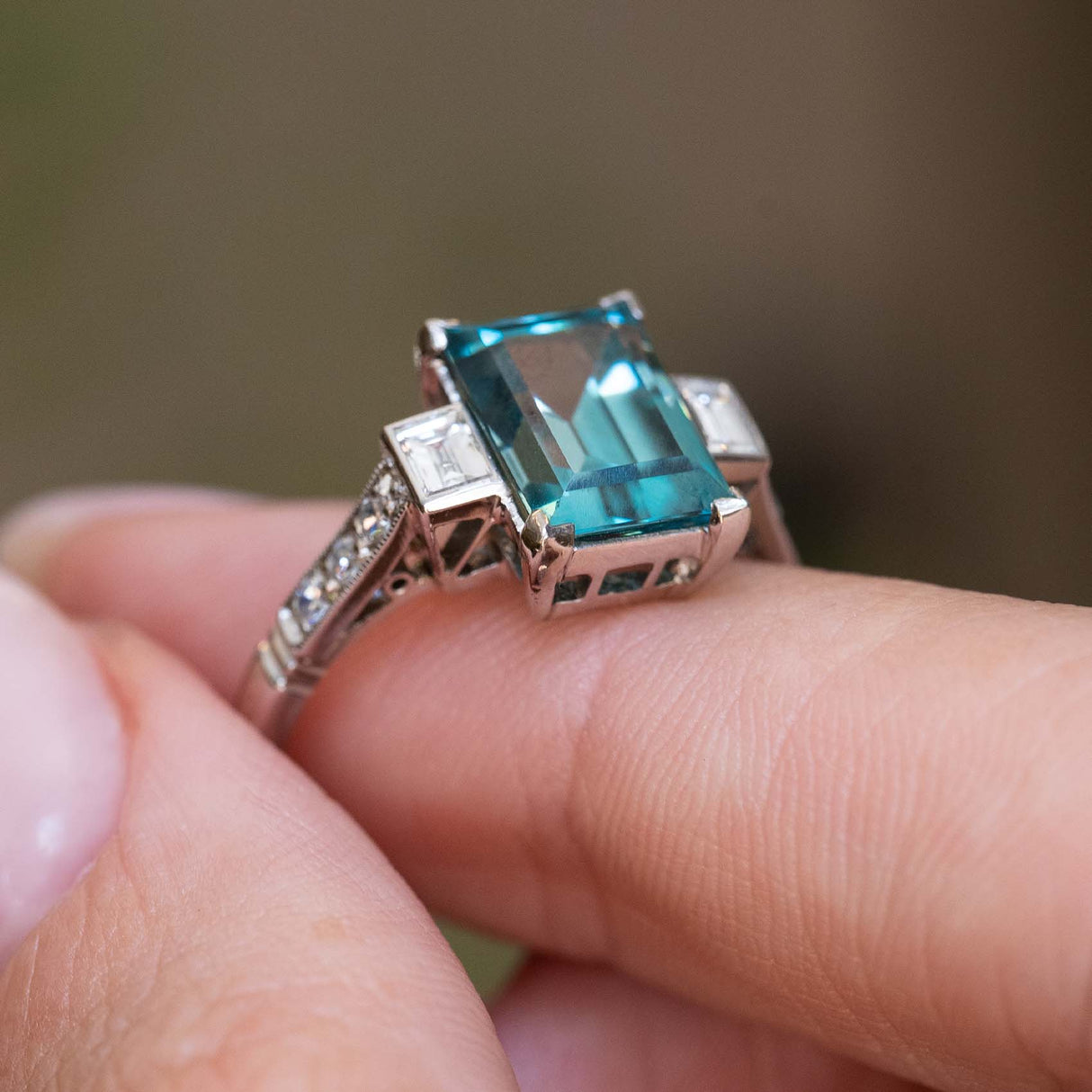 Side detail of an antique Art Deco 1920s zircon and diamond ring held between the fingers.