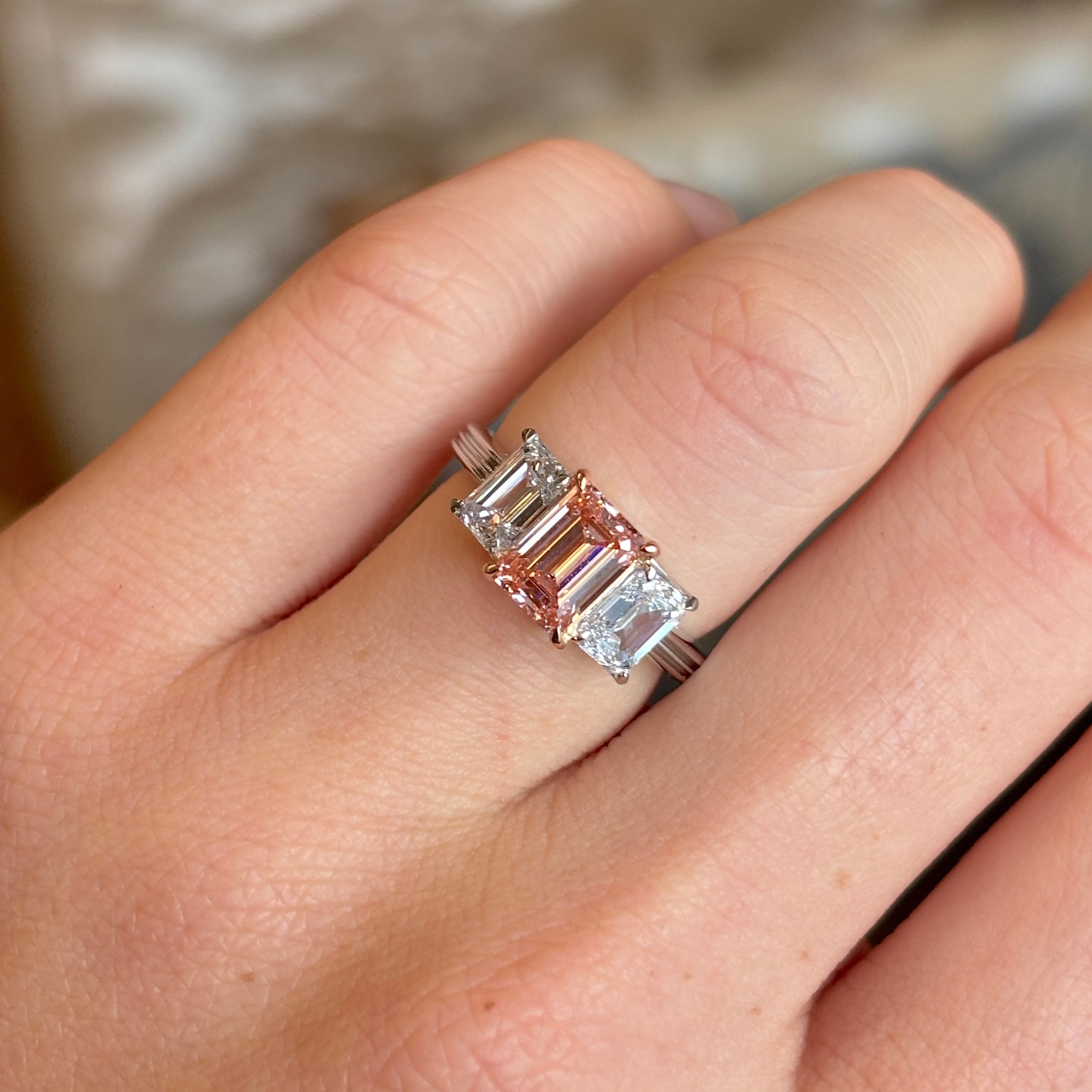 Lab-pink diamond and white diamond three-stone ring worn on the engagement ring finger, exhibiting the brilliance and presence when worn.