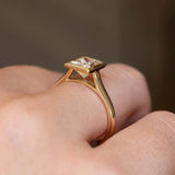 A close-up shot of a vintage-inspired princess-cut diamond engagement ring worn on a finger showing the minimalistic rub-over setting.