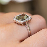 A close-up of the side view of a vintage-inspired, green cushion-cut sapphire and diamond cluster engagement ring in platinum.