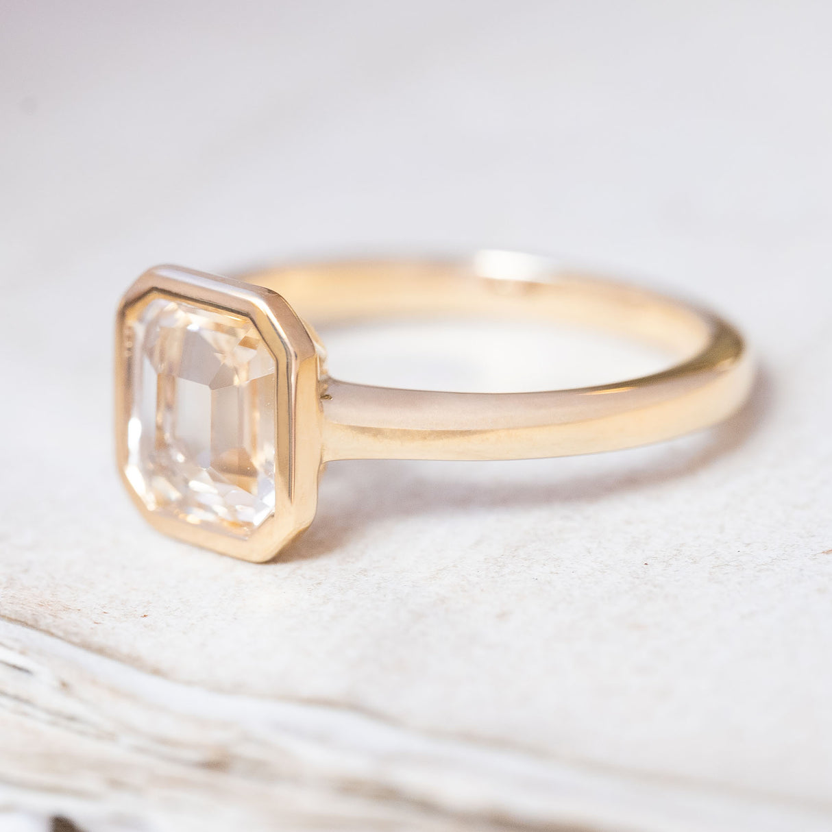A vintage-inspired, pale yellow sapphire solitaire engagement ring in yellow gold with a rub-over setting.