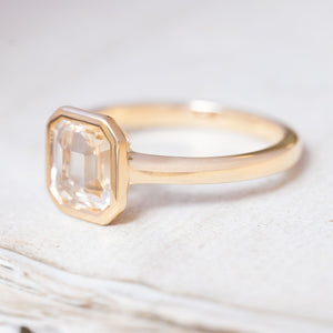 A vintage-inspired, pale yellow sapphire solitaire engagement ring in yellow gold with a rub-over setting.