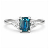 A close-up photo of a vintage-inspired, blue-green sapphire and diamond cluster trefoil engagement ring in platinum.
