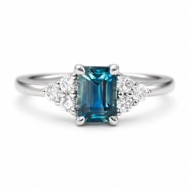 A close-up photo of a vintage-inspired, blue-green sapphire and diamond cluster trefoil engagement ring in platinum.