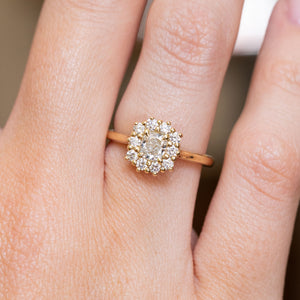 A close-up of an antique-inspired cushion-cut diamond halo engagement ring in yellow gold worn on a hand.