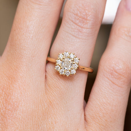 A close-up of an antique-inspired cushion-cut diamond halo engagement ring in yellow gold worn on a hand.