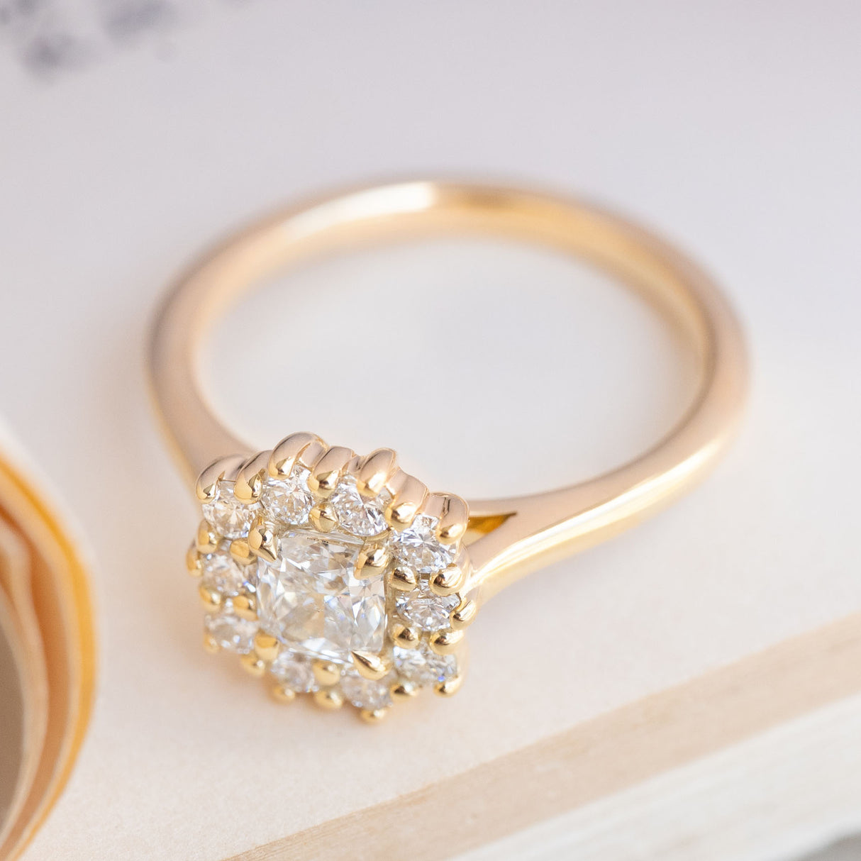 Vintage-inspired cushion-cut diamond engagement ring in yellow gold with a diamond cluster of round brilliant-cut diamonds.