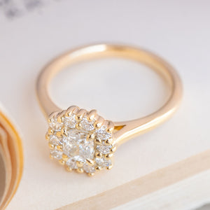 Vintage-inspired cushion-cut diamond engagement ring in yellow gold with a diamond cluster of round brilliant-cut diamonds.