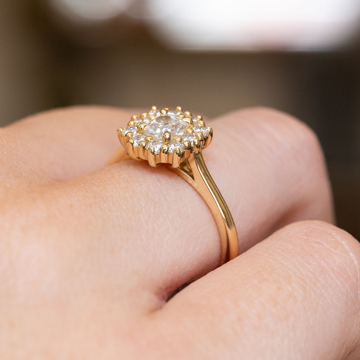 A close-up of a yellow gold ring with a cushion-cut diamond cluster worn on a finger. 