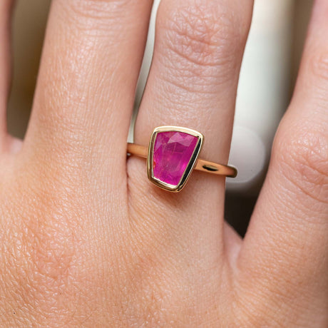 A gold ring with a rectangular faceted pink ruby, shown worn on a person's finger.