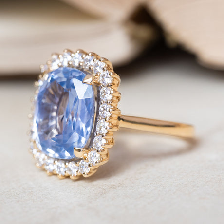 An antique-inspired cornflower blue sapphire and diamond cluster ring in yellow gold viewed from a three-quarter angle.