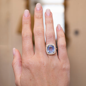 An antique-inspired light blue sapphire and diamond cluster ring in yellow gold worn on the hand.