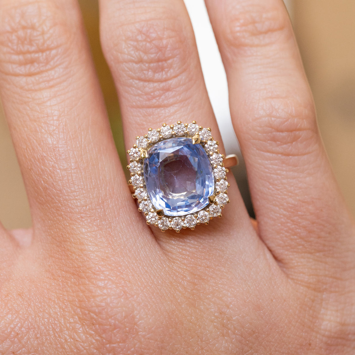 An antique-inspired blue sapphire and diamond halo cluster ring in yellow gold worn on the finger.