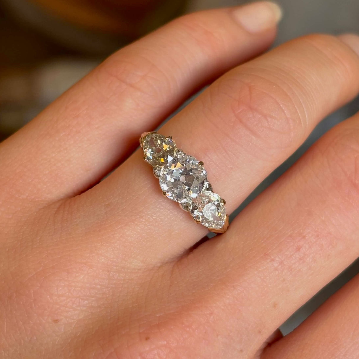 Antique Victorian three-stone with cushion-cut and pear-cut diamonds ring worn on ring finger close up