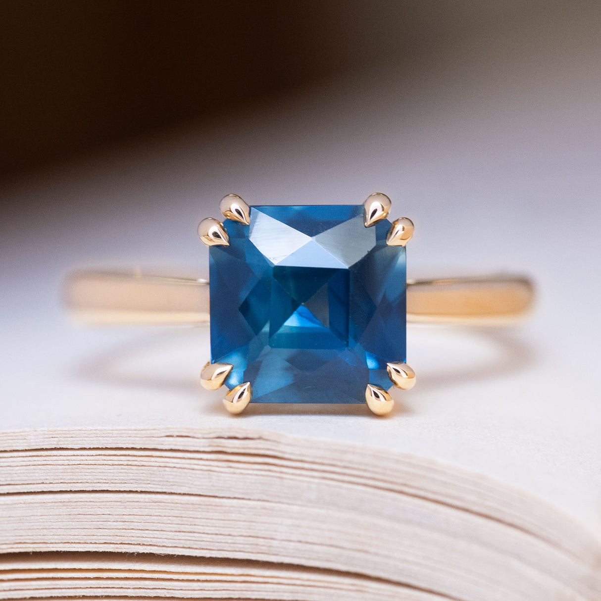 An antique-inspired deep teal square-cut sapphire solitaire ring in yellow gold.