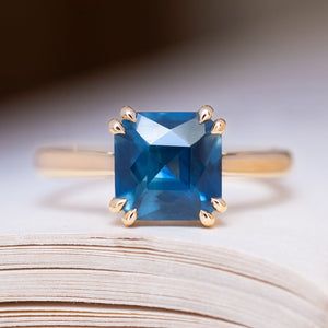 An antique-inspired deep teal square-cut sapphire solitaire ring in yellow gold.