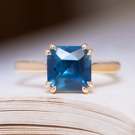 An antique-inspired deep teal square-cut sapphire solitaire ring in yellow gold.