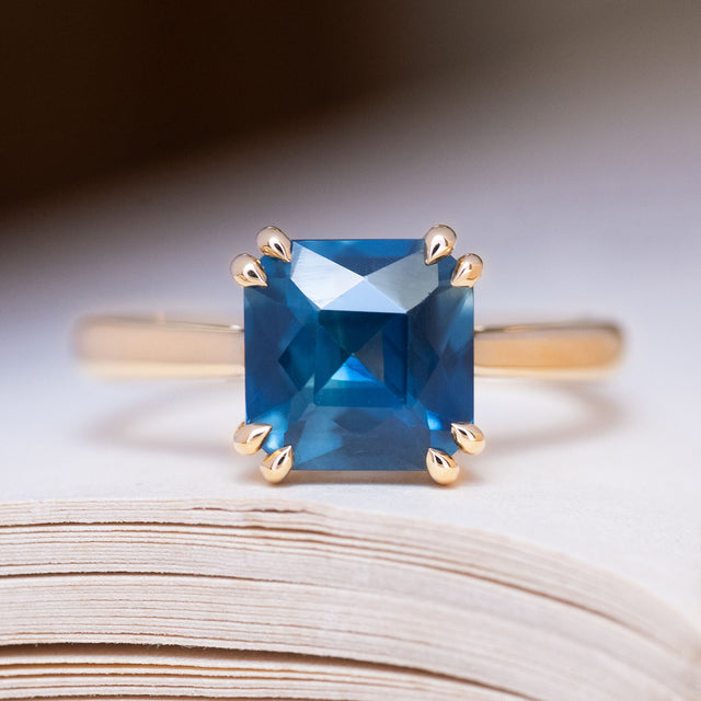 An antique-inspired deep teal square-cut sapphire solitaire ring in yellow gold.