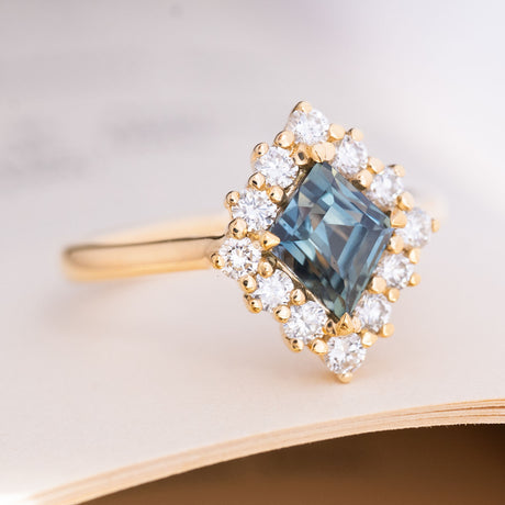 A vintage-inspired, blue kite-cut sapphire and diamond halo cluster engagement ring in 14ct yellow gold.