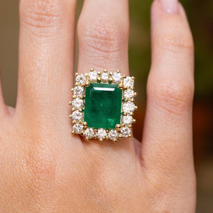 A vintage inspired emerald and diamond cluster ring in yellow gold worn on a hand. 