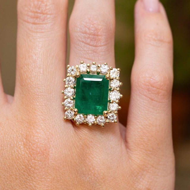 A vintage inspired emerald and diamond cluster ring in yellow gold worn on a hand. 