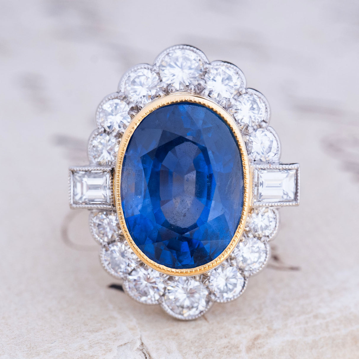 A vintage natural sapphire and diamond halo cluster ring in yellow gold and platinum featuring a rub-over set oval sapphire with a millegrain diamond halo.