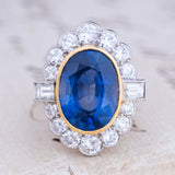 A vintage natural sapphire and diamond halo cluster ring in yellow gold and platinum featuring a rub-over set oval sapphire with a millegrain diamond halo.