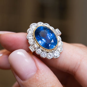 A vintage natural sapphire and diamond halo cluster ring held between the fingers.