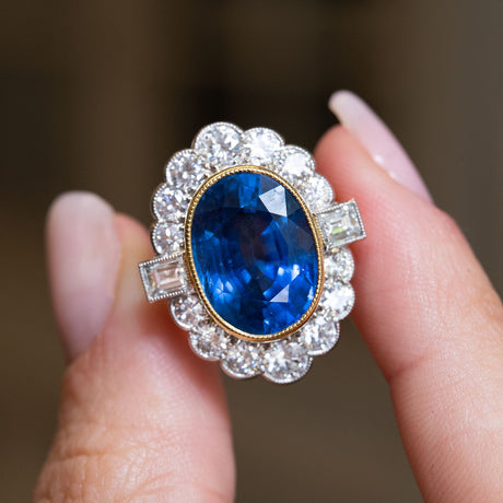 Close-up of a vintage natural blue sapphire and diamond halo cluster ring featuring an oval natural sapphire and brilliant-cut diamond halo.