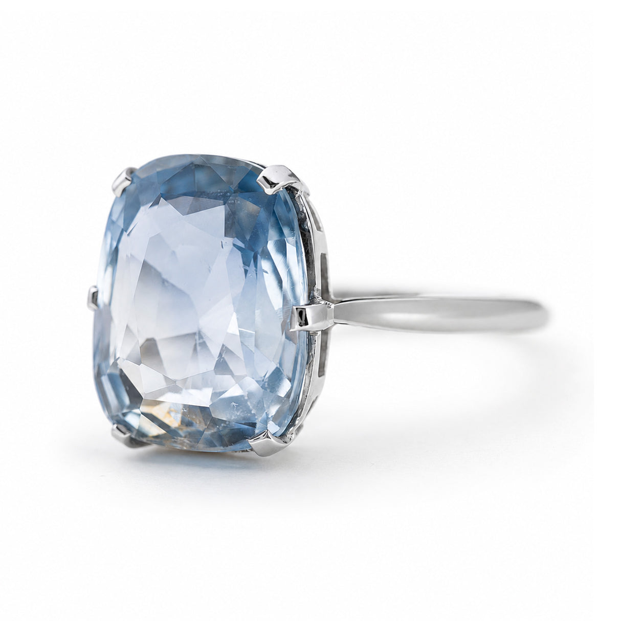 A platinum ring featuring a large cushion-cut light blue sapphire, shown on a clean white background turned partially to show the side.