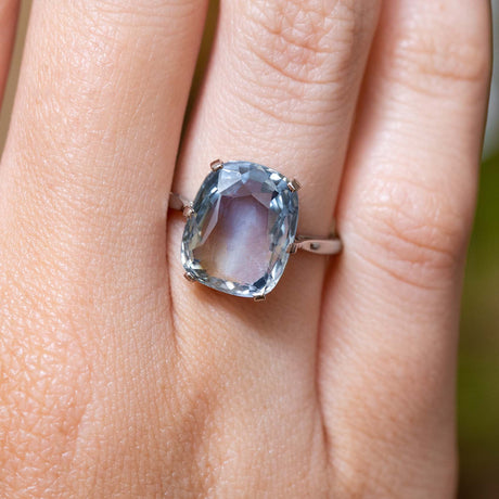 A close up photo of a large pale blue sapphire single-stone ring worn on the finger.