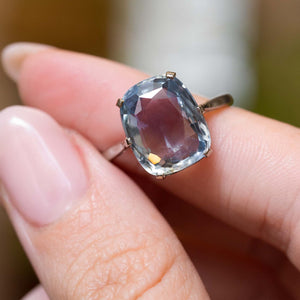 The sapphire solitaire ring held between fingers.