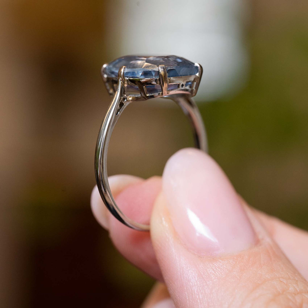 the sapphire ring held between fingers and turned sideways to show the gallery of the ring.