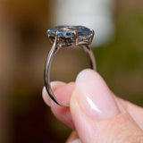 the sapphire ring held between fingers and turned sideways to show the gallery of the ring.