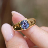 A close-up of an antique Victorian colour-change sapphire gypsy ring held between the fingers showing green, blue and purple hues.