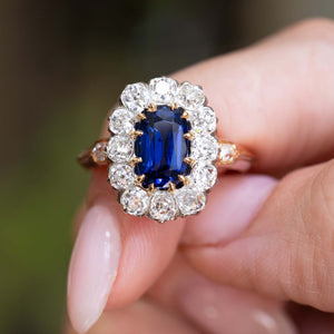 Close-up of an antique Jugendstil royal-blue sapphire and diamond cluster ring held between the fingers.