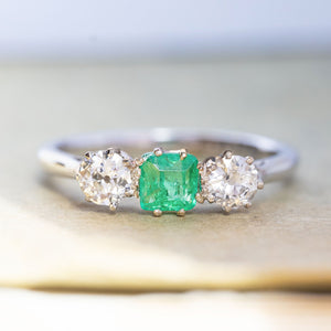 An antique, Art Deco emerald and old-cut diamond three-stone ring in white gold and platinum.