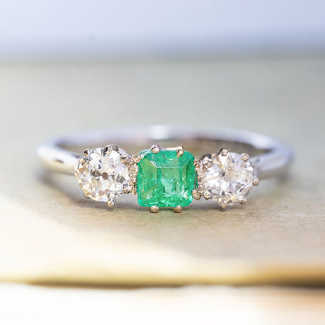 An antique, Art Deco emerald and old-cut diamond three-stone ring in white gold and platinum.